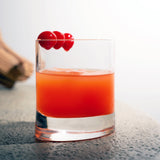 Veronese Whiskey Glass filled with orange cocktail and garnished with three cherries standing on a light surface
