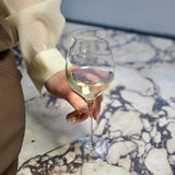 Hand holding a Vinea Malvasia wine glass filled white with wine on a marble surface