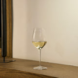 Vinea Malvasia wine glass filled with white wine on a wooden surface and a ivory background