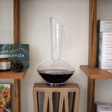 Vinea wine decanter filled with red wine standing on a side table and various items on shelves around it