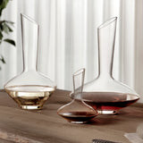 Three different sizes of Vinea wine decanters filled with wine, standing on a wooden table and a light background