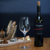 Empty Vinoteque Red Wine Glass standing next to a red wine bottle on a wooden table, behind is a blurred cheese board and a dark background