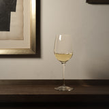 Crescendo Chardonnay White Wine Glass filled with white wine standing on a dark wooden surface, a neutral colors background and a golden picture frame