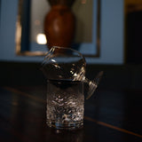 Vinoteque Cognac Glass filled with Cognac laying down in an angle on a DOF glass with warm water on a dark wooden surface