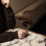 Hand holding Crescendo Bordeaux Red Wine Glass filled with red wine on a marble table and a dark background