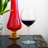 Vinoteque Robusto Red Wine Glass filled with red wine standing an a dark surface with colorful vase in the background
