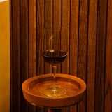 Vinoteque Riserva Red Wine glass filled with red wine and standing on a small wooden side table, wooden wall in the background