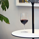 Vinoteque Riserva Red Wine Glass filled with red wine standing on a small white table a plant is in the background