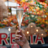 Hand holding a Vinoteque Flute Glass filled with sparkling wine on a fall themed colorful background