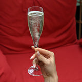 Hand holding a Vinoteque Flute Glass filled with sparkling wine on red background