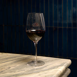 Vinoteque Ricco wine glass filled with red wine standing on a marble surface with a drack background