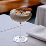 Milkshake with whipped cream and a cookie on top, served in a glass on a table.