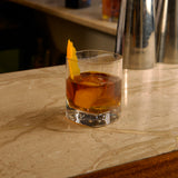 Glass of whiskey with an orange peel on a marble countertop