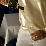 Person pouring white wine into a glass with a blurred background