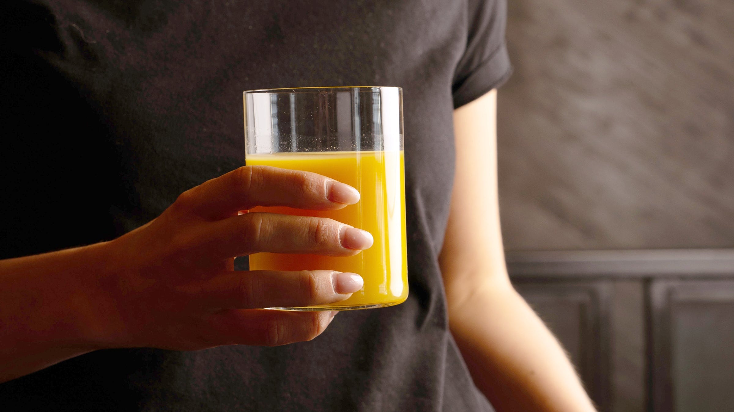 Top Class glass with orange beverage held in hand on a black background 