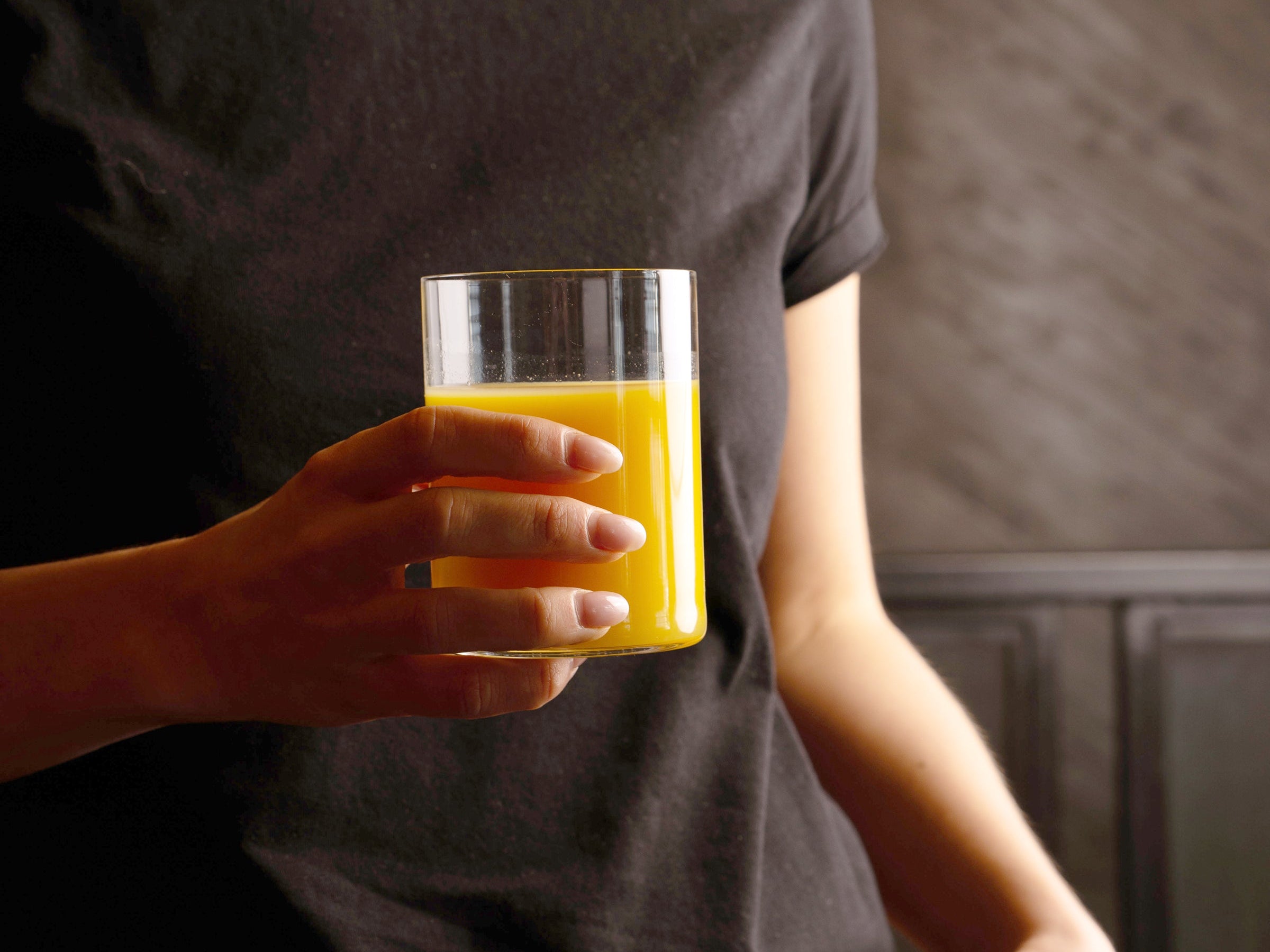 Top Class glass with orange beverage held in hand on a black background 