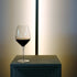 Atelier Cabernet wine glass filled with red wine standing on a white surface and a long lamp in the background