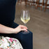 Hand holding Atelier Chianti wine glass filled with white wine on a dark blue velvet sofa