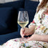 Hands holding Atelier Chianti wine glass filled with white wine on a floral dress background