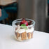 Lock-Eat Canning & Food Jar XL filled with an appetizing dessert of cream, cookies and finished with a miniature caramelized apple, chocolate chunks and a leaf, standing on a white surface