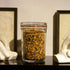 Lock-Eat jar filled with legumes standing on a black reflective surface and frames and hand sculptures in the background