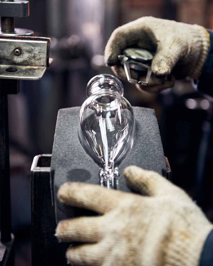 Person wearing gloves holding a glass bulb in a workshop setting