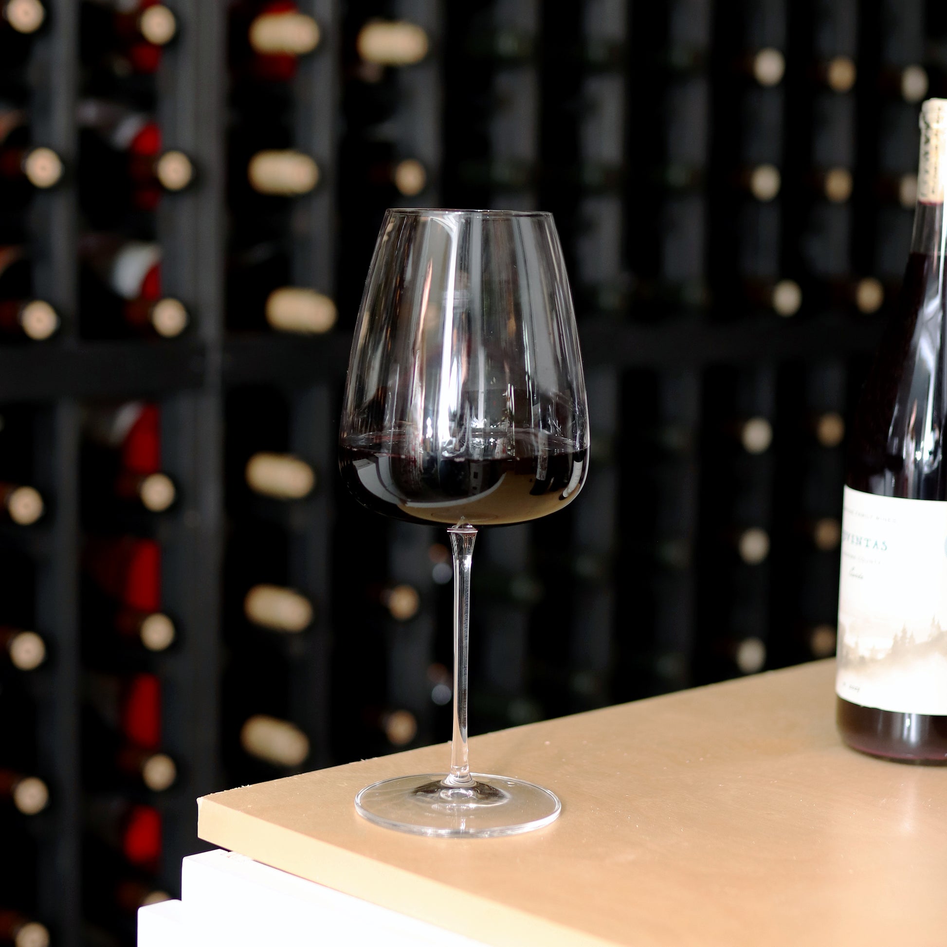 Talismano Italian Premium Bordeaux Red Wine Glass filled with a red wine standing on a wooden surface in a win cellar