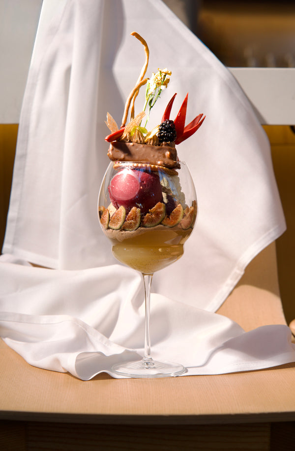 Gourmet dessert in a wine glass with decorative elements on a white cloth