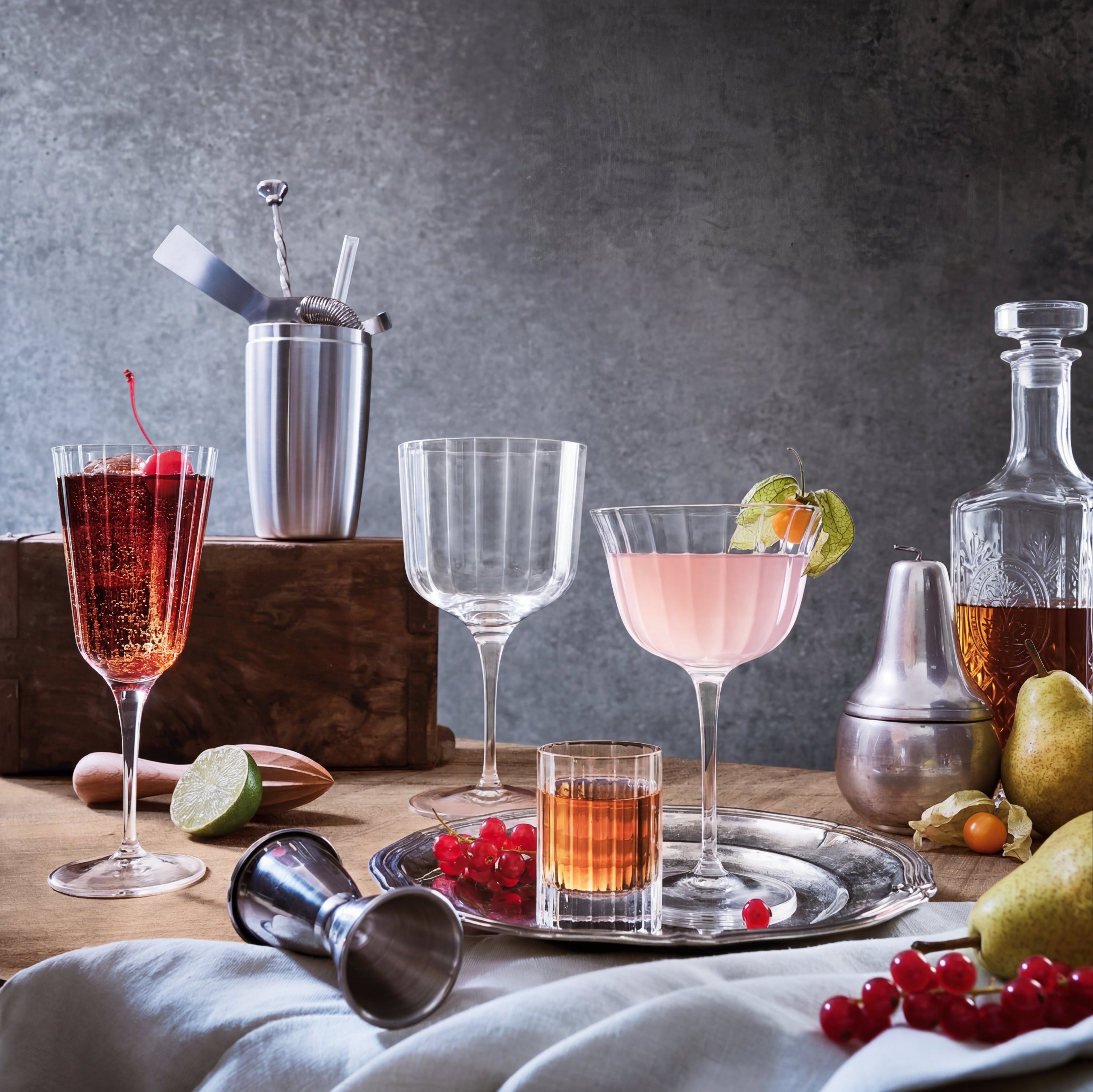 Cocktail setup with various glasses, bottles, and ingredients on a wooden table.