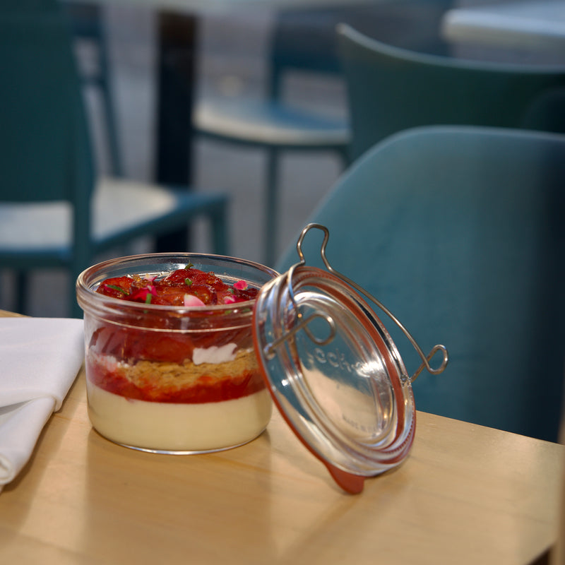 Small layered dessert in a glass jar on a table with chairs in the background