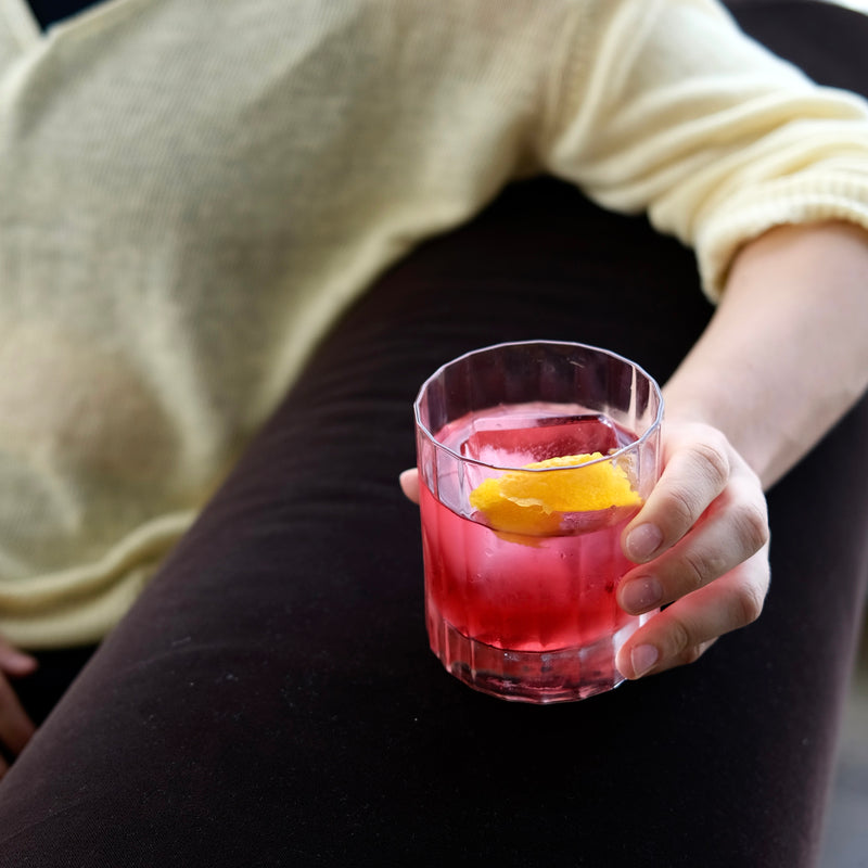 Person holding a pink non-alcoholic cocktail with a lemon twist in a clear glass.