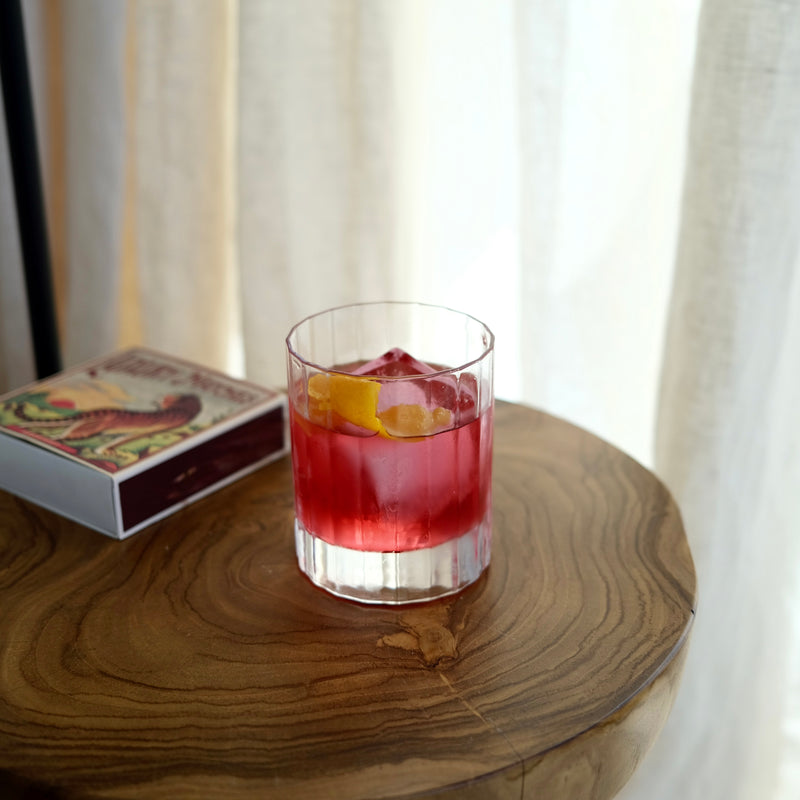 Clear glass with red non-alcoholic cocktail on a wooden surface next to a box of matches.