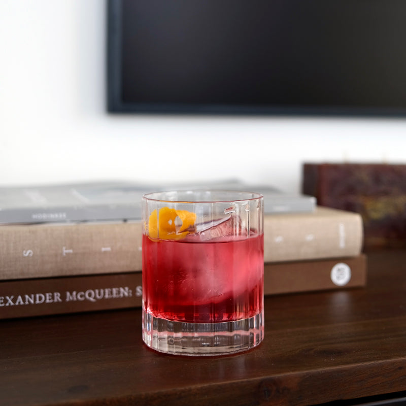 Red non-alcoholic cocktail in a glass with a yellow fruit on a wooden surface with books in the background