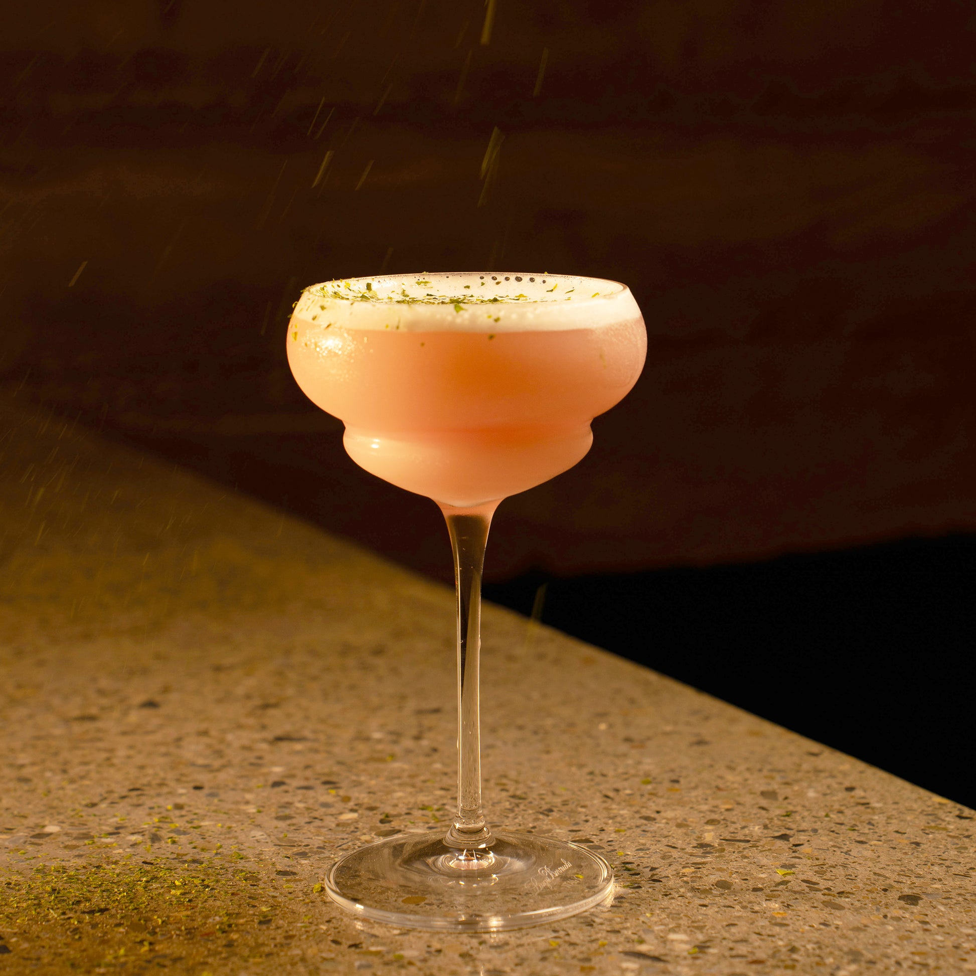 Backdoor '20s Italian Premium Nick & Nora Cocktail glass filled with a pink cocktail and garnished with line zest standing on a marble surface and a dark background
