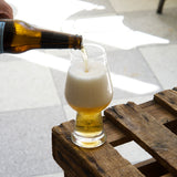 Beer being poured from a bottle into a glass on a wooden crate with a blurred background