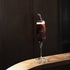Crescendo Flute Glass filled with a deep purple cocktail garnished with lavender standing on a thin wooden surface and a dark background