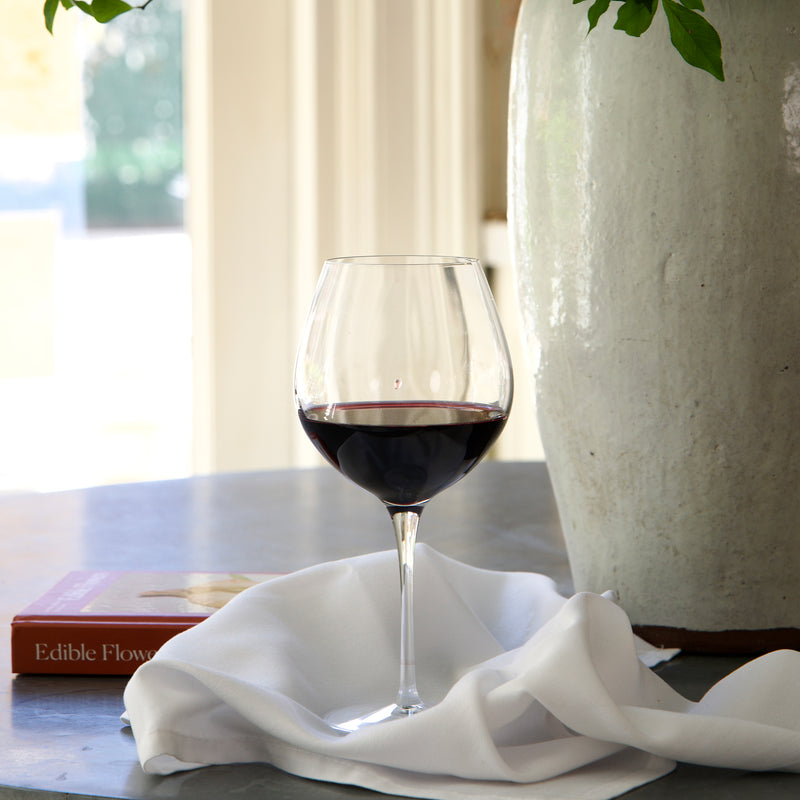 Wine glass with red wine on a table next to a vase and book