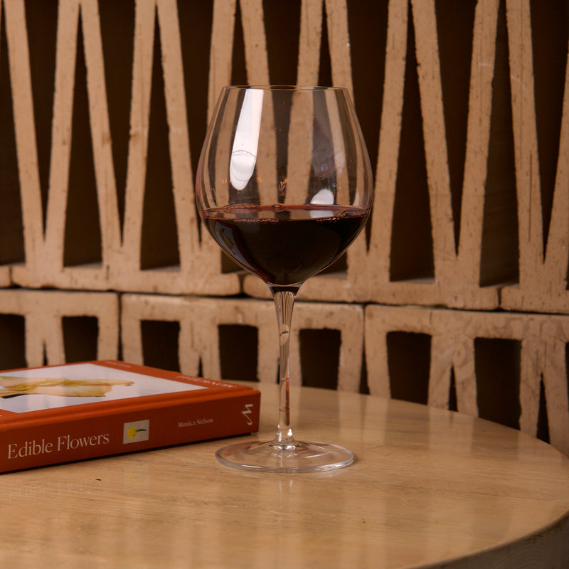 Wine glass with red wine on a wooden table next to a book titled 'Edible Flowers'.
