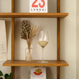 Wooden shelf with a glass of white wine, decorative vase, and calendar on a neutral wall.