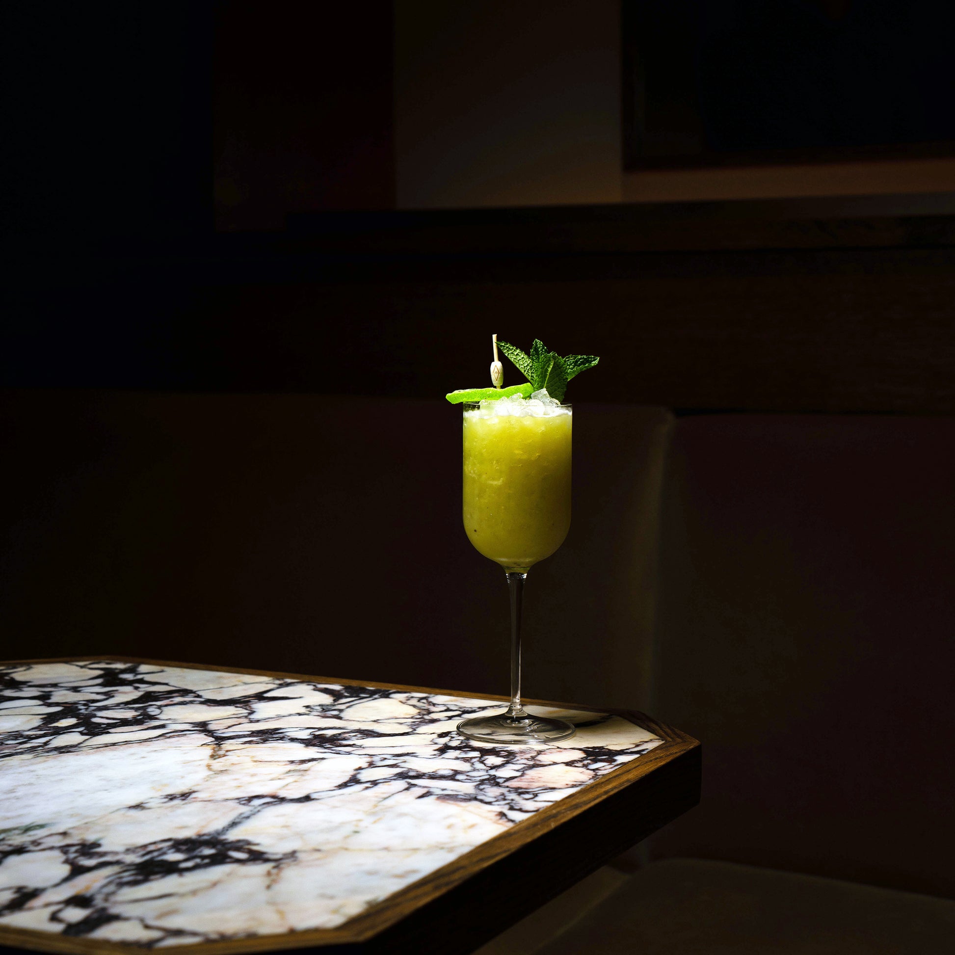 Jazz Negroni Cocktail Glass filled with bright green cocktail and garnished with mint leaves standing on a marble surface and a dark background