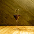 Magnifico large wine glass filled with red wine standing on a wooden table and a dark green background