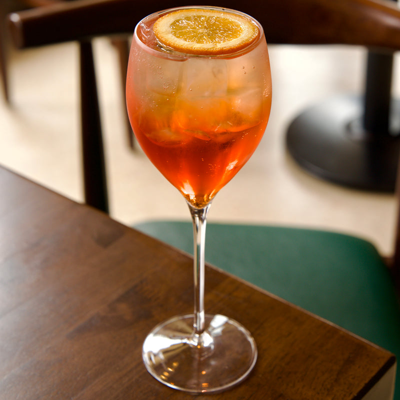Spritz cocktail with a slice of orange in a Magnifico Small glass on a wooden table
