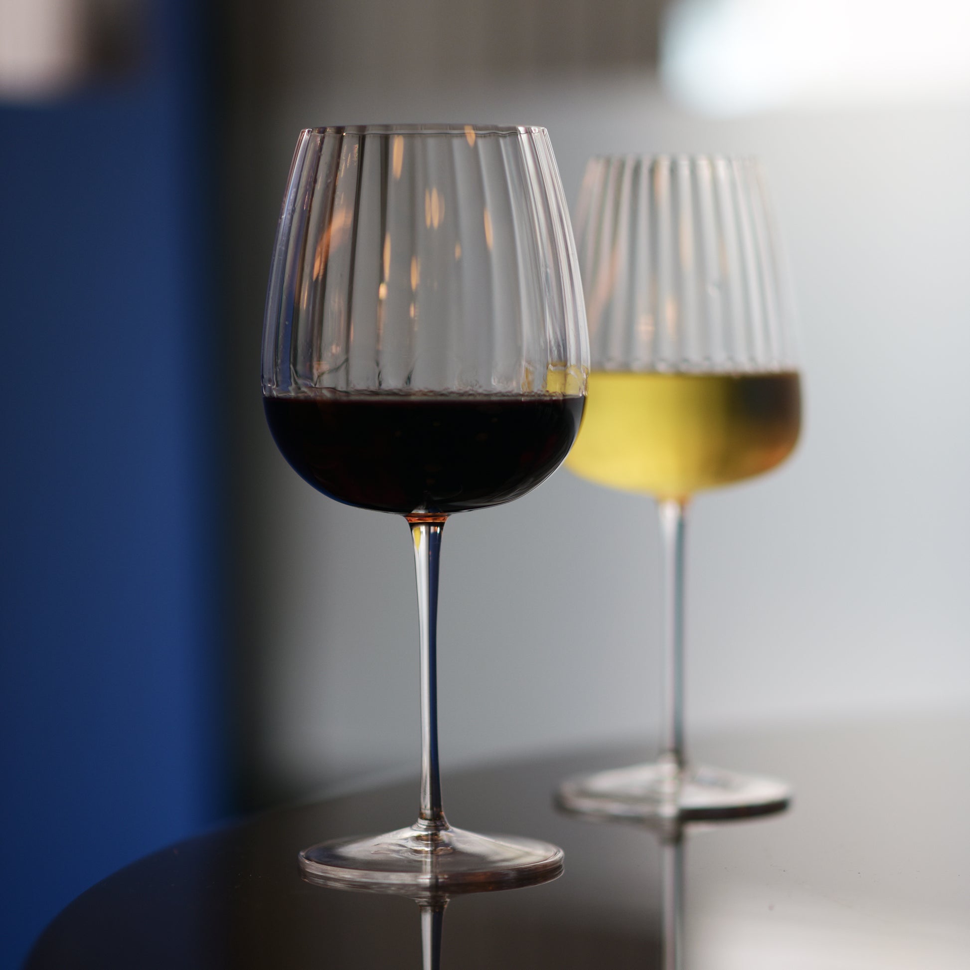 Gin & Tonic Jenever Gin glass filled with red wine standing on a dark surface, blurred white wine glass filled with white wine in the background