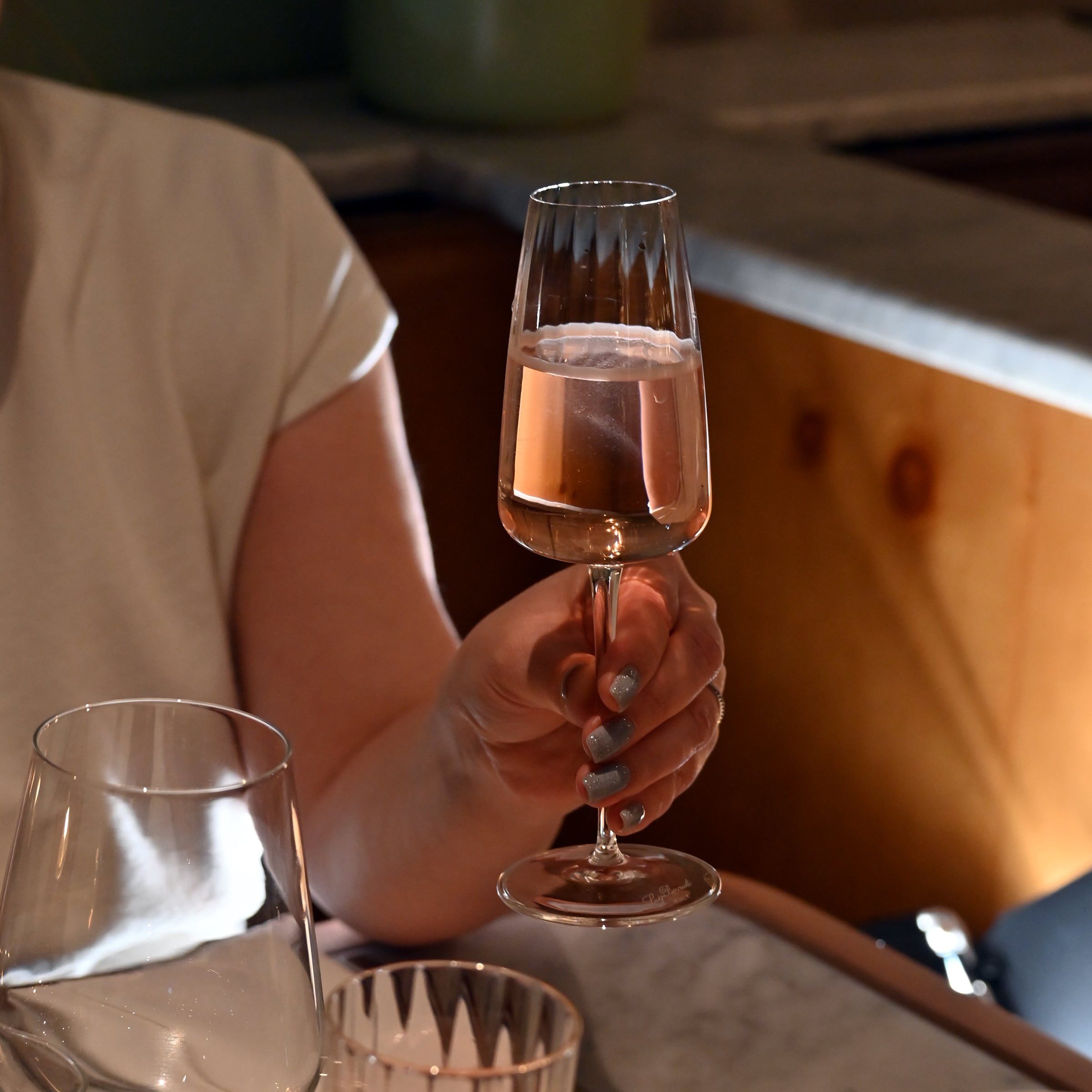 Hand holding an Optica Prosecco flute filled with Rose wine in a soft restaurant setting 