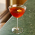 Cocktail in a Optica Martini glass with an orange twist on a green marble surface