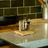 Sublime DOF glass filled with water standing on a coaster kitchen counter with various items in the background