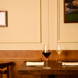 Two wine glasses on a wooden table with a beige wall and framed picture in the background