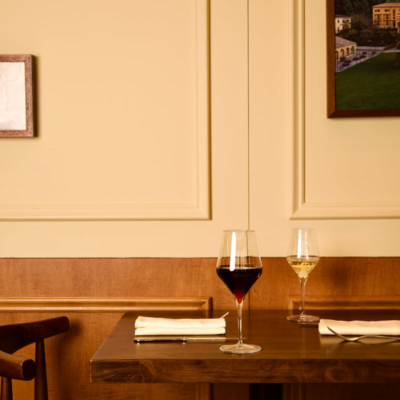 Two wine glasses on a wooden table with a beige wall and framed picture in the background