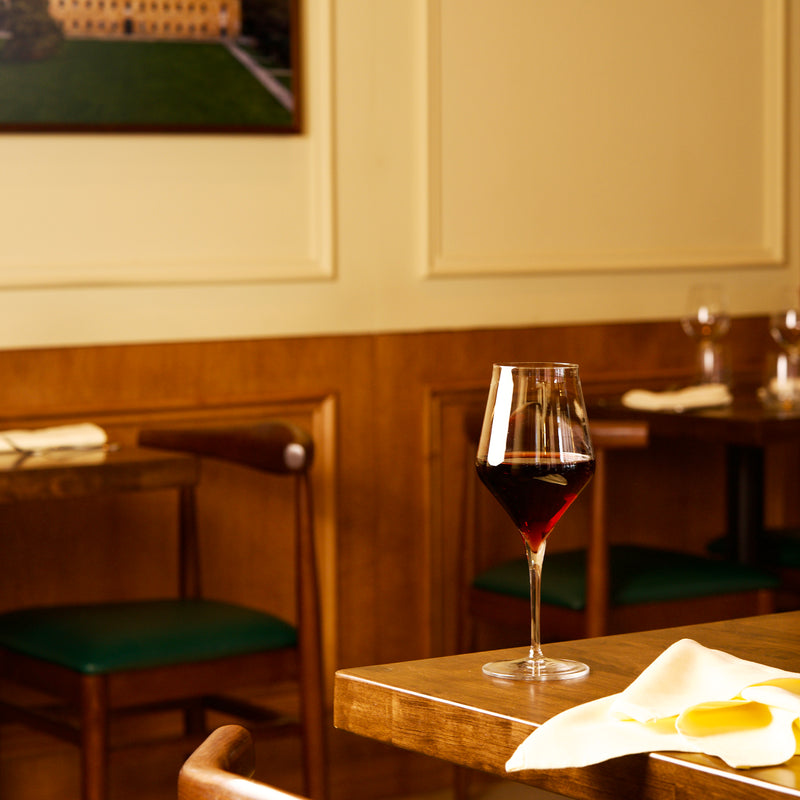 Supremo Bordeaux wine glass on a table filled with red wine in a cozy restaurant setting