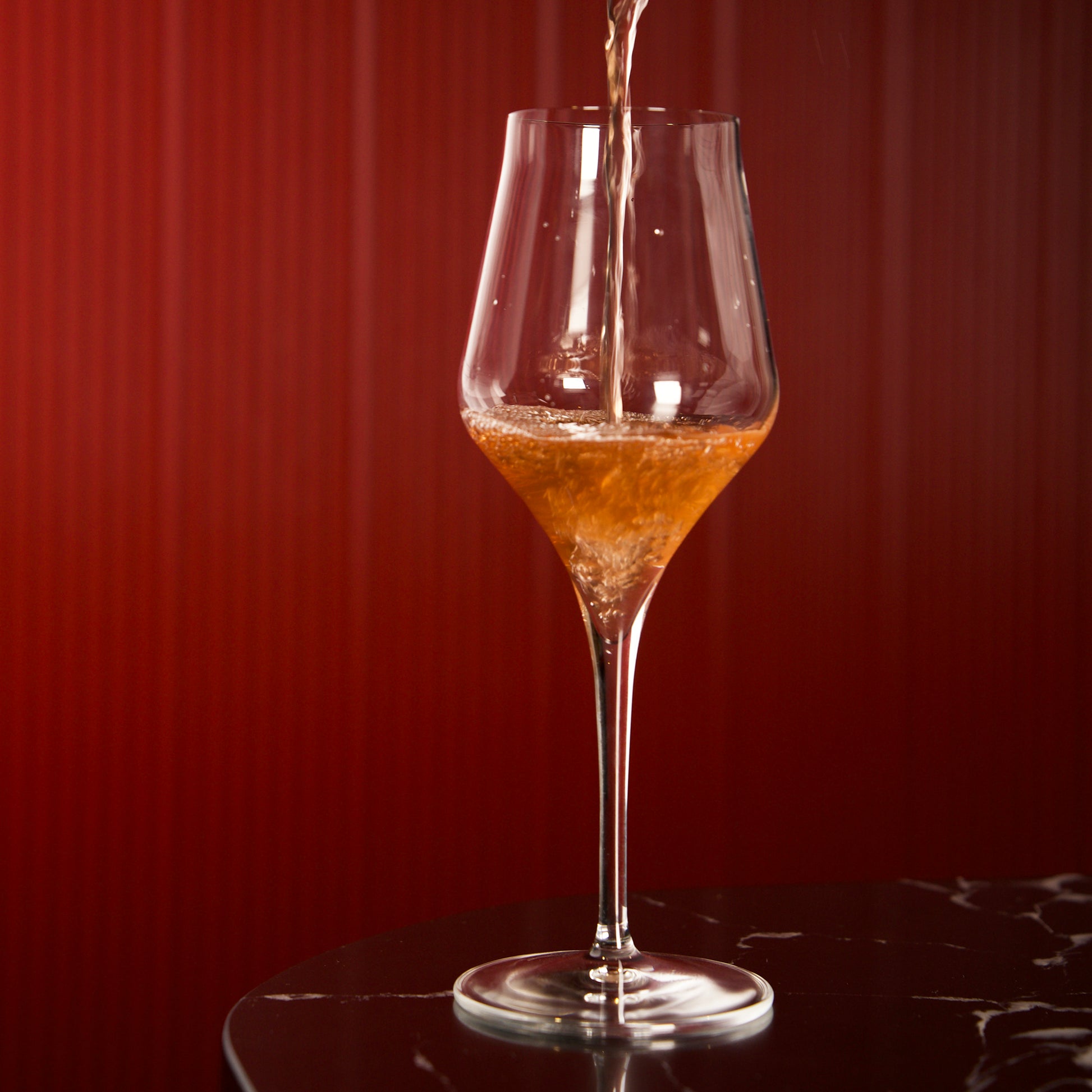 Supremo Chardonnay wine glass being filled with orange wine against a dark background